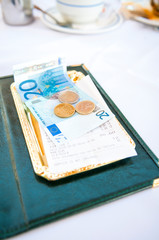 Obraz premium Tray of euro notes and coins sitting in a tray on an outdoor table with a nondescript restaurant receipt in Portuguese