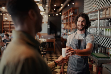Smiling mature waiter giving take away coffee to man at cafeteria