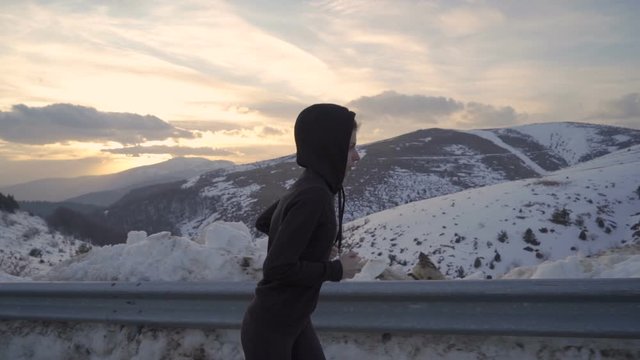 Concentrated fitness girl running, sprinting in cold winter day in the mountains at golden sunset