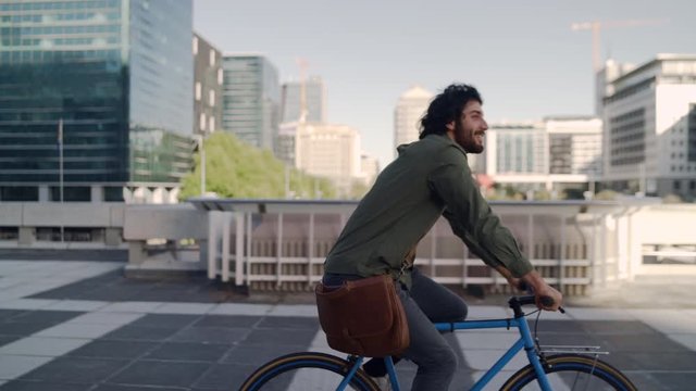 Successful smiling professional young man riding bicycle in front of modern buildings at background
