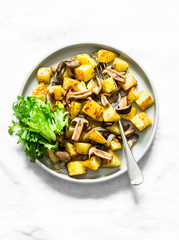 Fried potatoes with mushrooms and green salad - delicious simple vegetarian lunch on a light background, top view