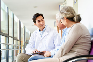 young asian doctor talking to senior couple patients in hospital hallway