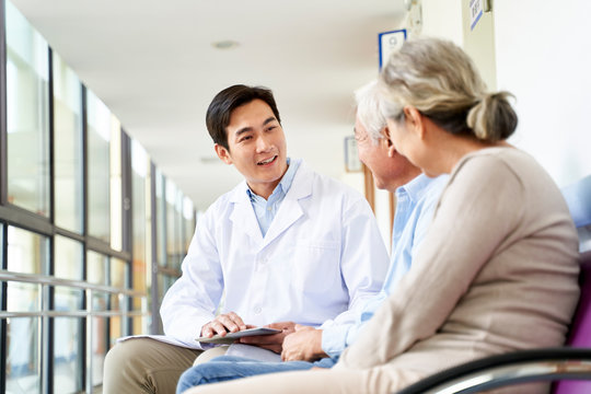 young asian doctor talking to senior couple patients in hospital hallway