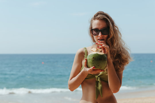 The girl with the coconut on the beach. Girl drinks coconut milk on the beach. High quality photo