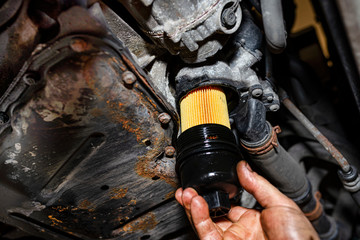 The car mechanic screws a new oil filter on the bottom of the engine.
