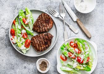 Beef medium rare steak and romaine salad cherry tomatoes yogurt dressing salad on a gray background, top view