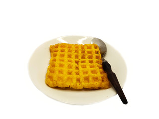 The bread is golden brown, shaped like a honeycomb in a slab with a soft dough texture. Has a sweet taste, placed on a white plate beside a spoon with a white background