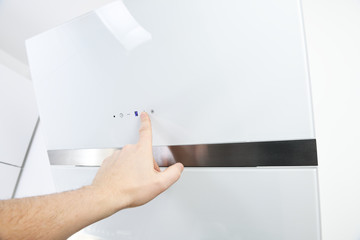 The male hand turns on the hood.Close-up of a touch control panel on a white glass kitchen hood.