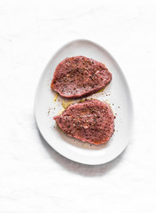 Raw marinated beef steak on a light background, top view