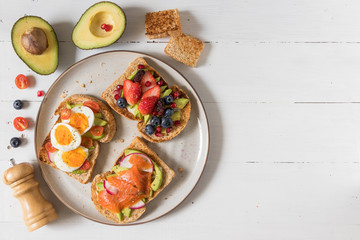 Avocado toast with different topping including salmon fish, eggs, berries, healthy and organic food, breakfast meal on white wooden background