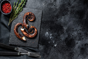 Fototapeta na wymiar Fried octopus tentacles with thyme and pink pepper. Fresh seafood. Black background. Top view. Copy space