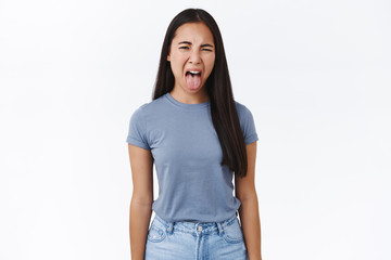 Disgusted asian young girl cringe from awful smell, sticking out tongue, squinting and wrinkle nose...