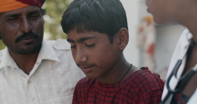 Young medical inter female student using a stereoscope to check the heartbeat of a young teenage male child in rural Rajasthan, India with his father being really concerned with the well being of kid