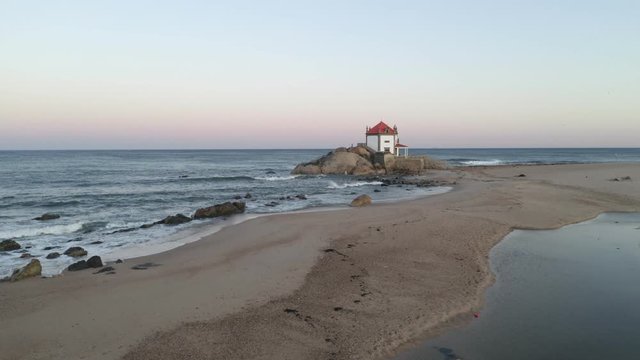 Capela Senhor da Pedra most beautiful chapel drone aerial view on a beach near the ocean, in Portugal