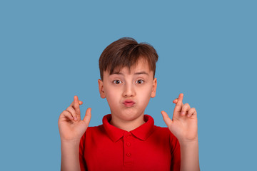 The young boy crossing his fingers making wishes against a blue background.