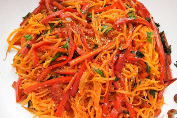 Slices of carrot and red sweet pepper are sauteing in a black frying pan