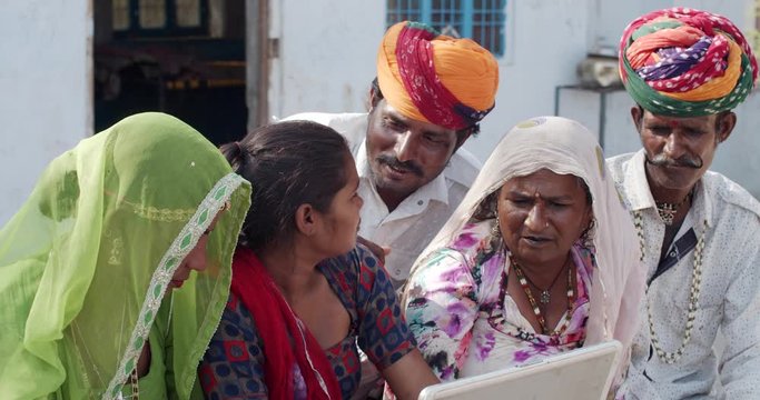 Young teenage daughter wither her mother, father and grand parents and teaches educates of portable laptop- dressed in traditional costumes from Rajasthan India- colorful turban and salwar kameez