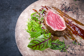Fried dry aged beef fillet medallion steak natural with lettuce and spice as closeup on a rustic modern design plate with copy space right