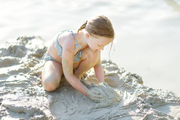 Young girl taking healing mud baths on lake Gela near Vilnius, Lithuania. Child having fun with mud. Kid playing with clay.