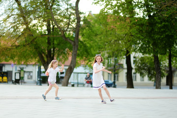 Two cute young sisters having fun together on beautiful summer day in a city. Active family leisure with kids.