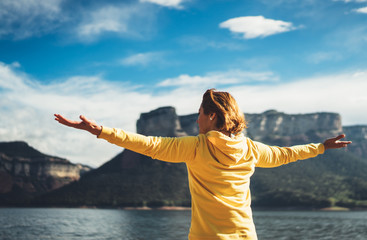 tourist traveler standing with raised hands, girl hiker enjoying mountains lake with arms outstretched breathing of fresh clean air in trip in spain, relax holiday