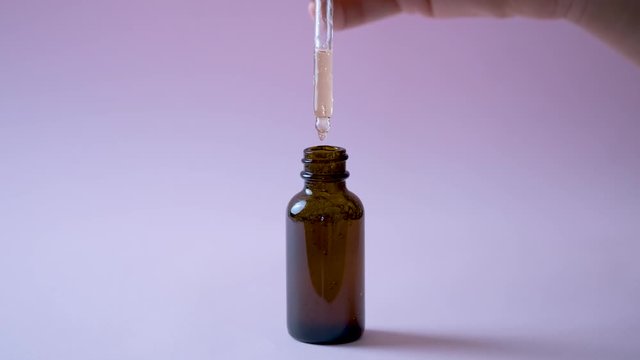 Young beautiful woman open dark brawn bottle with hyaluronic acid, cosmetic serum. Girl makes essential oil drops from cosmetic pipette in glass bottle. Beauty face skin care concept on pink backdrop.