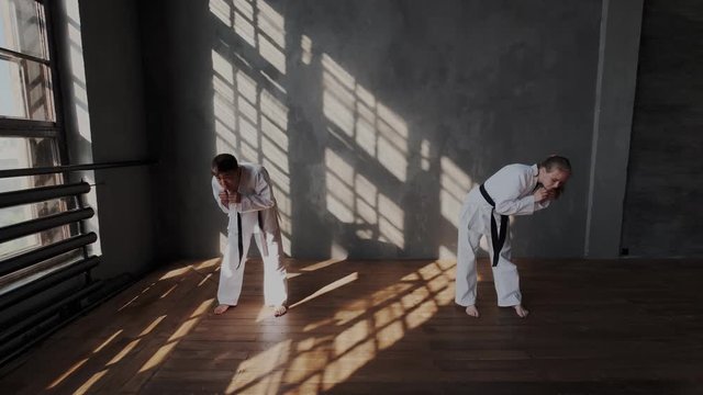 Slow motion. Dark-haired Korean boy and a european blonde girl warm up and stretching in training class. Multi ethnic teens practice Traditional fight arts indoor.