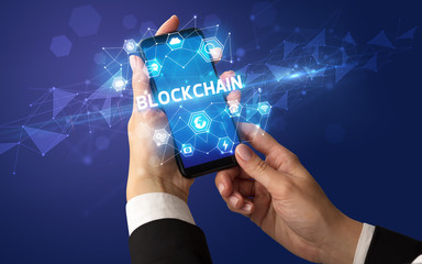 Female hand holding smartphone with BLOCKCHAIN inscription, modern technology concept