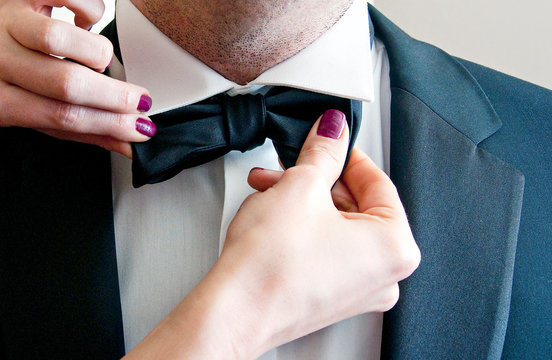 A woman's hand straightens the groom's bow tie