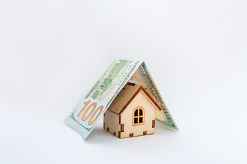 Financial growth concept, real estate tax, buying and selling houses, insurance. A miniature house and a banknote like a roof. Protect your house concept. Small toy house covered by dollars and euros