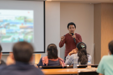 Asian Speaker is speaking on the stage over the presentation screen in the education seminar