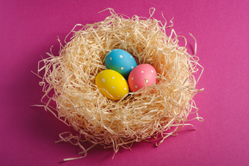 Colorful polka dot Easter eggs in wooden nest on pink purple plain background, greeting card, angle view