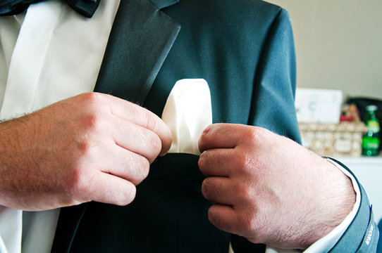 The Groom straightens white handkerchief on the collar of his suit