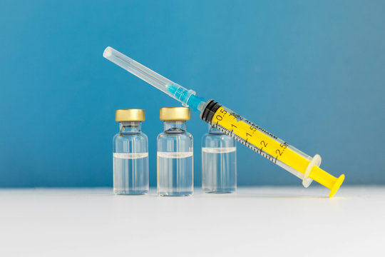 Glass vials with liquid and empty syringe on blue background. Coronavirus vaccine. nCov-2019 disease. Illness prevention. Medical injection. Flu shot drug. Baby vaccination. Healthcare and medicine th