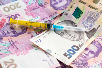 Syringe on pile of ukrainian banknotes. Sale of drugs, сocaine, heroin or ecstasy. Illegal business. Healthcare and medical concept.