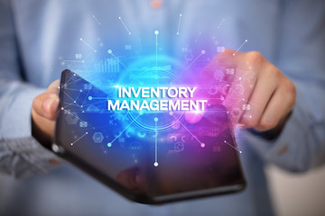 Businessman holding a foldable smartphone with INVENTORY MANAGEMENT inscription, new business concept