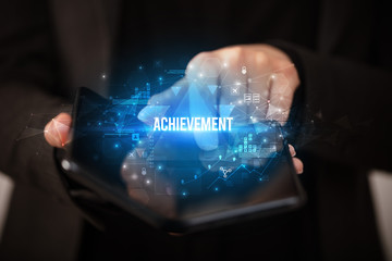 Businessman holding a foldable smartphone with ACHIEVEMENT inscription, business concept