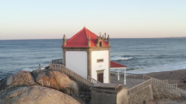 Capela Senhor da Pedra most beautiful chapel drone aerial view on a beach near the ocean, in Portugal