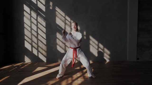 A young blonde girl shows punches and blows. Her hands are clenched into a fist, she moves quickly and breathes using special techniques. Practicing authentic martial arts.
