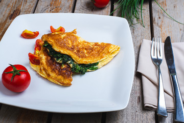 Traditional omelet with vegetables, spinach, tomatoes and herbs on a wooden table in a restaurant.