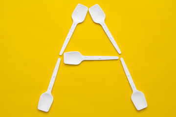 White plastic spoons in the form of letter A on yellow background. Top view. Copy, empty space for text