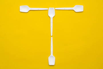White plastic spoons in the form of letter T on yellow background. Top view. Copy, empty space for text