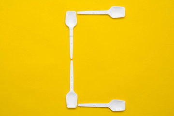 White plastic spoons in the form of letter C on yellow background. Top view. Copy, empty space for text