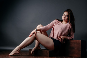 Fototapeta na wymiar Beautiful sporty young girl model posing on a gray background. Woman in sportswear shorts and a white top and in a pink sweater, looking at the camera