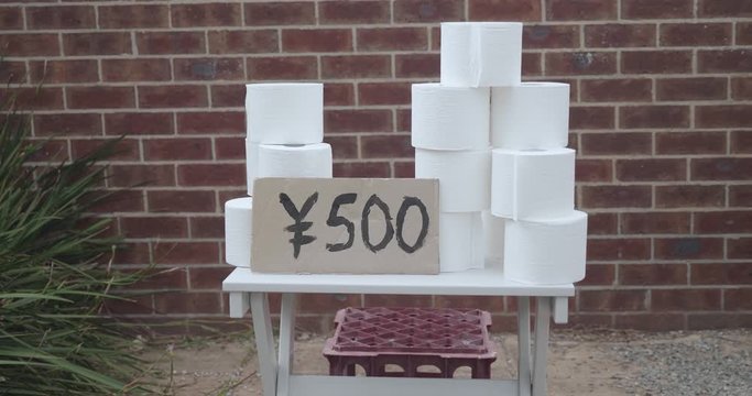 Children have a toilet paper stand outside of their house in Japan selling rolls of toilet paper taking advantage of a toilet paper shortage. There is a hand painted sign with 500 yen written on it