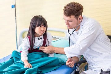 Obraz premium Pediatrician (doctor) man examining little girl patient using a stethoscope in hospital.
