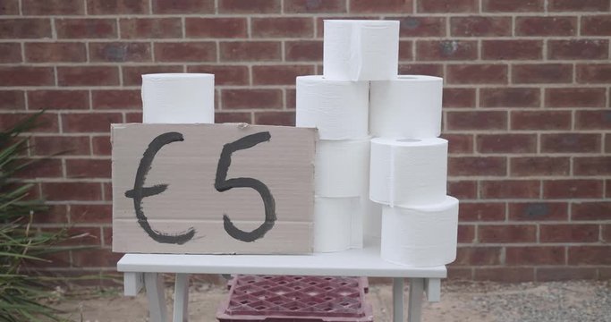 Children have a toilet paper stand outside of their house in Europe selling rolls of toilet paper taking advantage of a toilet paper shortage. There is a hand painted sign with five euros on it