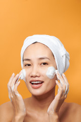 Laughing girl applying moisturizing cream on her face. Photo of young girl with flawless skin on orange background. Skin care and beauty concept