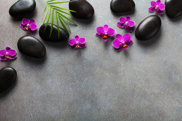 Fototapeta na wymiar Spa composition with flowers, green leaves and massage stone on gray background top view. Beauty treatment and relaxation concept. Flat lay. .