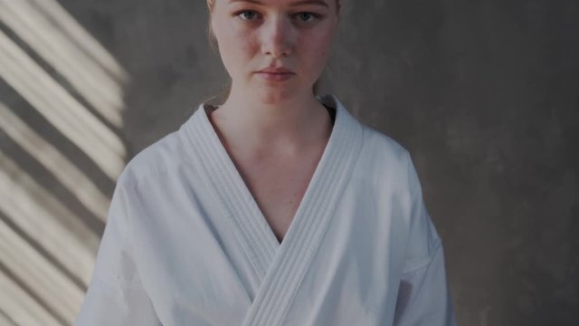 Close up. The girl tightens a black belt on a white kimono and looks up at the camera. Concentrated and focused serious female fighter ready for action and attack. Slow motion.